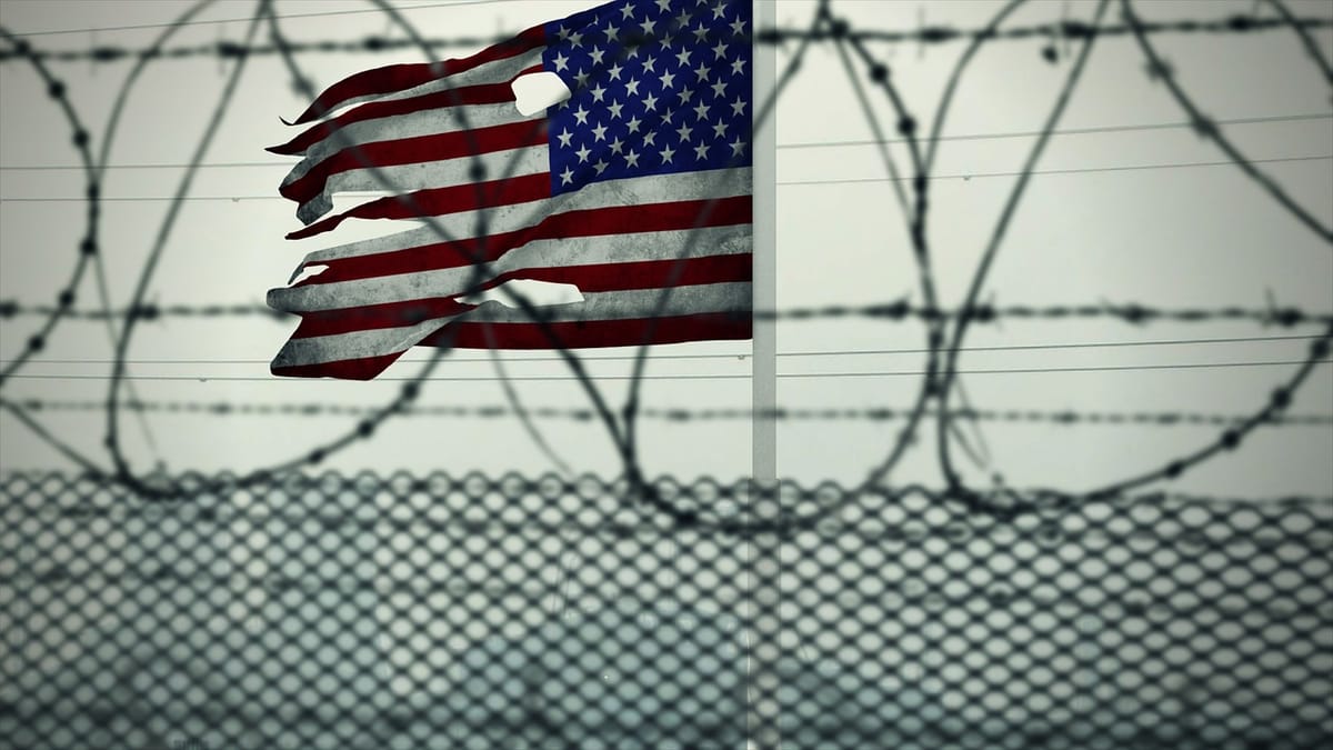 A tattered American flag behind a barbed wire fence