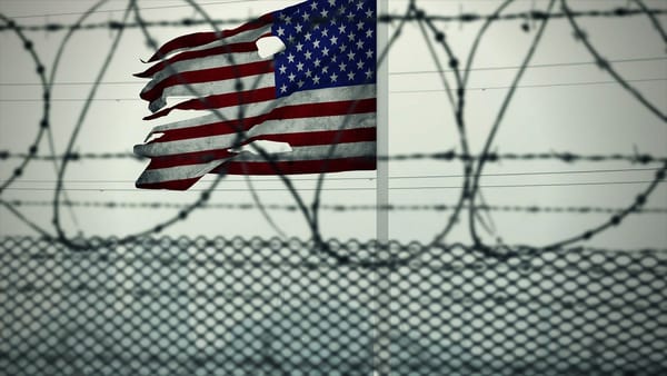 A tattered American flag behind a barbed wire fence